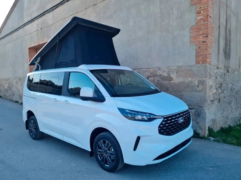 Van blanc équipé d'un toit relevable OVR déployé le long d'un mur en pierre